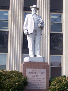 The white statue is larger than life, mounted on a pink granite base with an
elaborate engraved memorial; Everett wears a jacket that fails to cover a copious midsection.