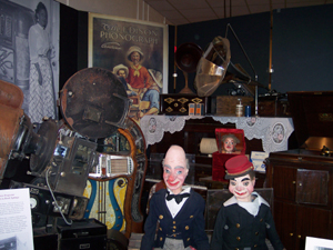 The photo shows puppets, musical instruments, and furniture