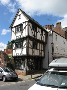The first floor overhangs the ground floor by two feet, the second floor overhangs the first floor by another foot or two, and the attic and roof appears to overhang a little bit more; the building is in white with dark brown painted timbers.