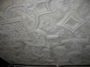 The elaborate plaster ceiling is carved in a repeating pattern in bas-relief, with protrusions extending downward