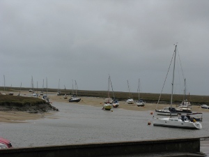 The inlet curves around, with just a little water left at low tide; some of the boats are beached.  The sand is tan, the river and sky brownish gray, the land flat and featureless and dark greenish brown