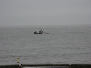 Looking terribly alone in the gray sea beneath a gray sky, a small trawler works the beach off Lowestoft