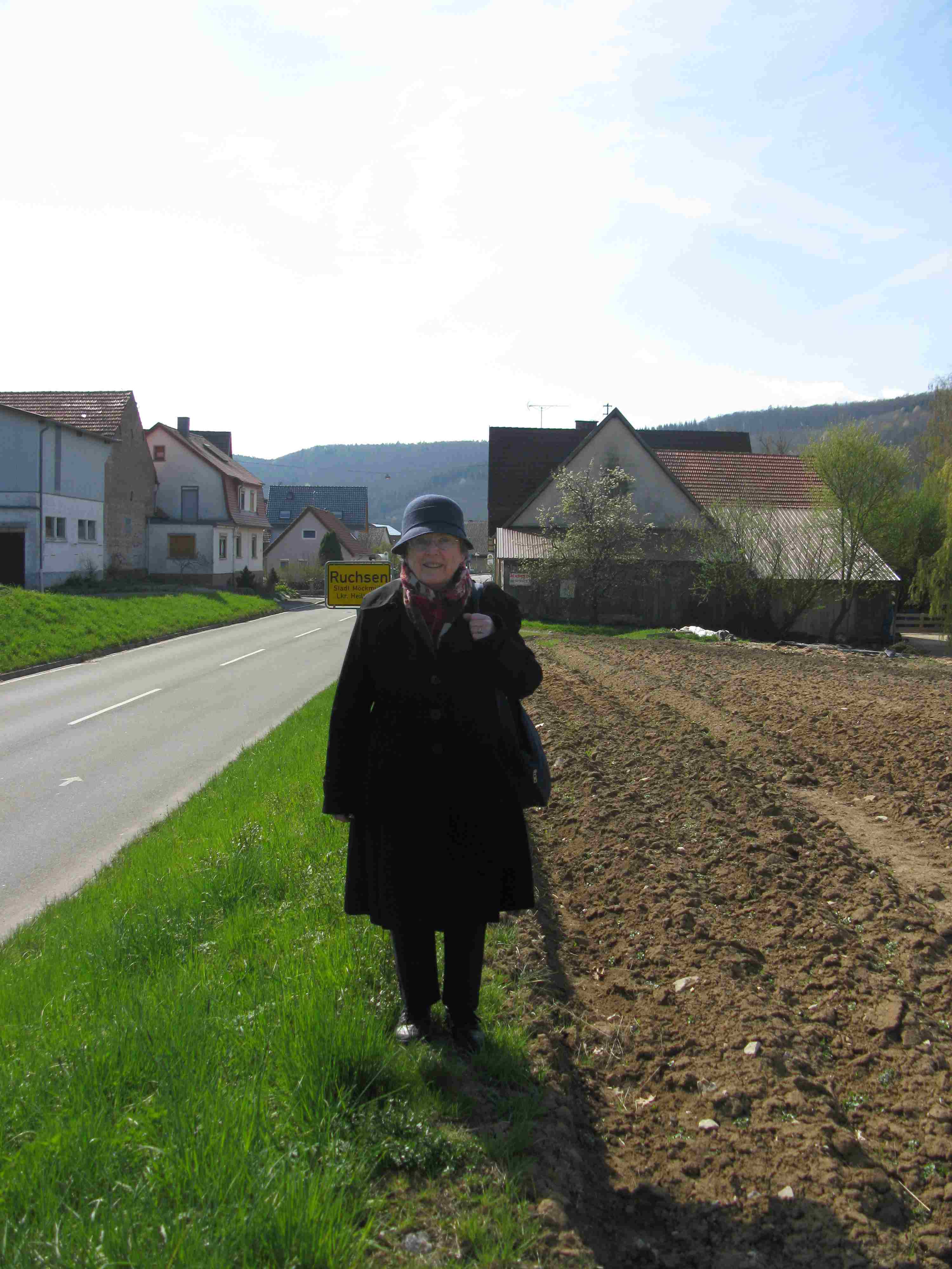 Elsa stands by the side of the road with the houses of the village of Ruchsen behind her