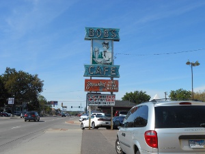 The tall sign features four sections, the second of which depicts an old-time carhop