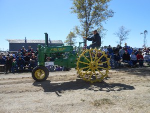 An old John Deere tractor with a green body and bright yellow steel wheels having pointed lugs to grip the ground
