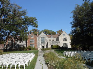 The picture shows the back of the house, seen from the garden, where white chairs have been set out for a wedding