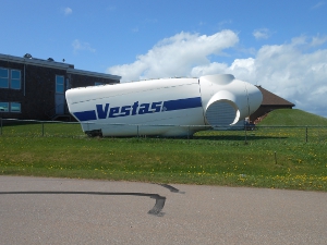The body of a wind power generator rests on the ground in a static exhibit, it is white and almost as big as an automobile