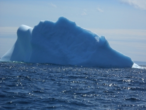 The iceberg is triangular in shape (above the water) and makes a stark contrast to the surrounding water.