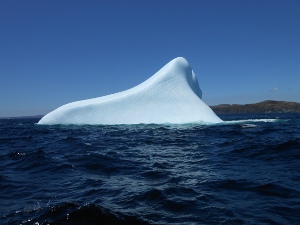The iceberg is triangular in shape (above the water) and makes a stark contrast to the surrounding water.