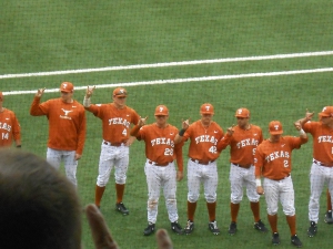 set off in white pants along with burnt orange socks, shirts, and caps, with the longhorn emblem, the University of Texas players hold up their hands in the 'Hook 'em horns' salute.