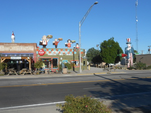 On the roof of the store are four statues of declining size of people holding up hamburgers of similarly declining size. A rooster statue is next door, pepper and Uncle Sam statues are on the sidewalk to the right.