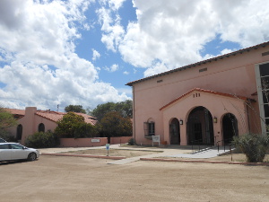 A two-story pink stucco building set against a sky filled with white clouds against a blue background