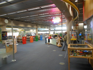 Brightly colored stacks of childrens books, display cases, neon ceiling signs, and a spacious floor area make the interior of the library functional and appealing.