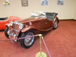 The classic red two-seater roadster has plenty of shiny chrome and glass in front, and gleaming wire wheels.  The rear view mirrors are mounted on the fenders.