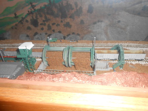 The model depicts the car with two rotating cylindrical drums dumping earth and rock fill into the dam