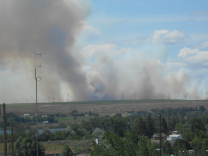 Dark brownish-gray plumes of smoke billow up into the sky marking the location of the grass fire.
