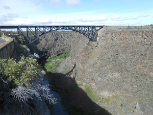 Staying at the level of the plateau, the black iron bridge arches over the steep grey stone sides of the gorge.