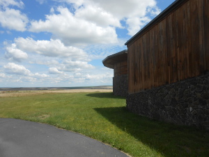 The photograph reveals the windowless walls of the museum on the right, while puffy clouds mark the blue sky over the flat plateau of the Columbia basin.