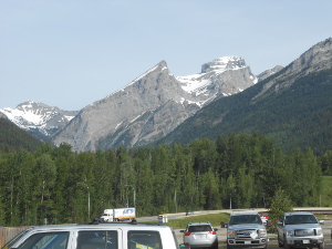 A snow-capped double peak in the distance, with hills covered with coniferous trees in the foreground