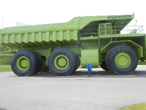 The huge ore carrier truck has three axles and a pale green dump truck body.  Elsa stands at the side, about one third the height of a wheel