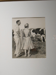 This old black and white photograph shows the farmer and the queen standing side by side looking at dairy cattle.
