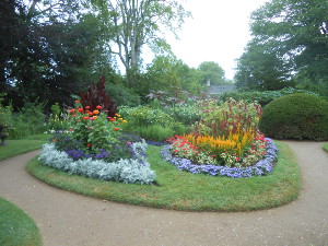 The garden path surrounds an oval of green grass, inside of which are three different floral displays, using contrasting colors to create a painter's pallette