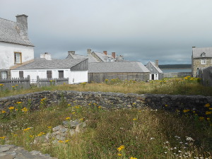 In the foreground a rectangular stone wall indicates the location of a house not rebuilt, while half a dozen town buildings in grey and white form the background.