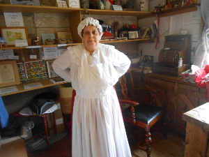 Hands behind her back, the guide is wearing a white dress covered by a white apron and a white cap