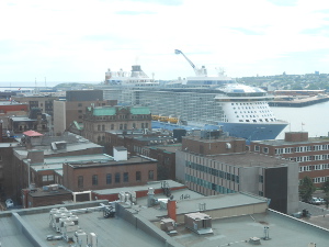Tied up to the dock, the massive cruise ship towers over the buildings along the waterfront.  The picture, taken from a hotel window, shows many rooftops in the foreground with the ship behind.