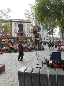 In a round public plaza, a juggler on stilts handles flaming batons