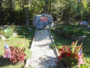 With pots of flowers in the foreground, a stone path leads back to a large rock on which is attached a brass plaque commemorating the exact time when President McKinley died and Theodore Roosevelt became president.