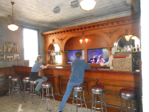 With bar stools in front for museum visitors to sit, the screens appear to be other drinkers sitting at the bar and talking