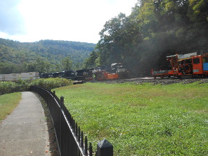 The black locomotives pull the train around the curve as the track workers pause to let the train pass