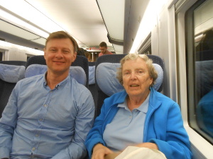 Elsa sits next to a tall young man dressed in a blue shirt on the comfortable high speed train