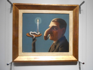 Magritte's painting depicts a man with his nose curving down into the bowl of the pipe he holds in his mouth, while the wax of a candle wraps around the candle stand like a snake