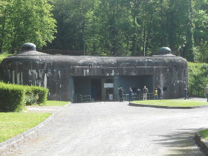 The dark grey exterior of the mostly underground defensive fortification looks uninviting against a background of green trees
