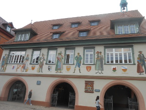 The house has figures of people in local dress along with coats of arms painted in between the windows on the first floor.