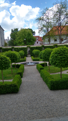 The garden is separated into four rectangular regions with a fountain in the middle; each region has a path, four corner miniature trees, and is surrounded by low square-cut boxwood hedges