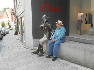 The statue is painted bronze; the soldier wears a black cap, black jacket with gold insignia, black boots, and white breeches, and is sitting on the stone wall.  Bob sits next to him, looking up