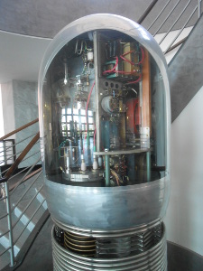 The top half of the Van de Graaf generator is visible on this floor, while the rest is a floor below.  It is cylindrical in shape, with a hemispherical top.  The apparatus is exposed to view.