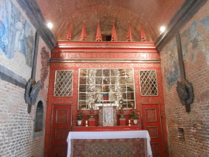 inside a recess, the chapel has a brightly colored and decorated red wall with a small altar in front