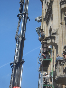 A long arm of a cherry picker crane extends into the sky next to the Rathaus lifing a statue out of its niche with a cable