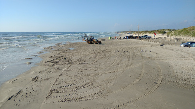 On a Corpus Christi beach a high loader shifts sand back into the ocean, near the line of fishermen's parked cars