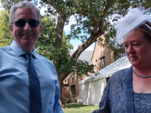 With a white tent shaded by a tall tree in the background, Bryan wears sunglasses, blue shirt and a (very rare for him) dark blue tie, while Donna is clad in a blue dress with a white fascinator.