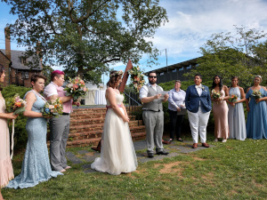 Emily's brother Dan stands in front of the gathering and reads a selection for the wedding, with members of the bridal parties standing left and right.