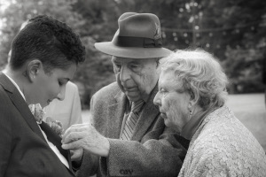 A black and white photograph, with Bob and Elsa at right and Carmen at left; Bob is fastening the pin which holds Carmen's boutonniere to her jacket
