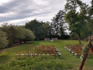 The seats for the wedding guests are empty on the green lawn, while in the distance the brides and the wedding party are gathering to start the ceremony