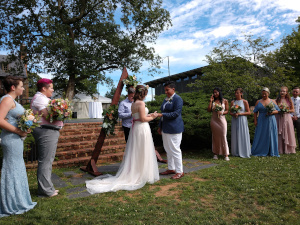 The brides are standing facing one another, awaiting the arrival of the bridesmaids to tie their hands together, one ribbon at a time, until they are eternally bound