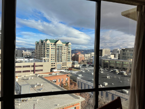 Beneath a partly cloudy sky and through a clear glass window pane, the view covers several high rises and building roofs