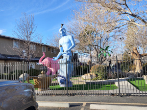 Behind a wrought iron fence stand sculptures of a pink elephant and a pale blue genie